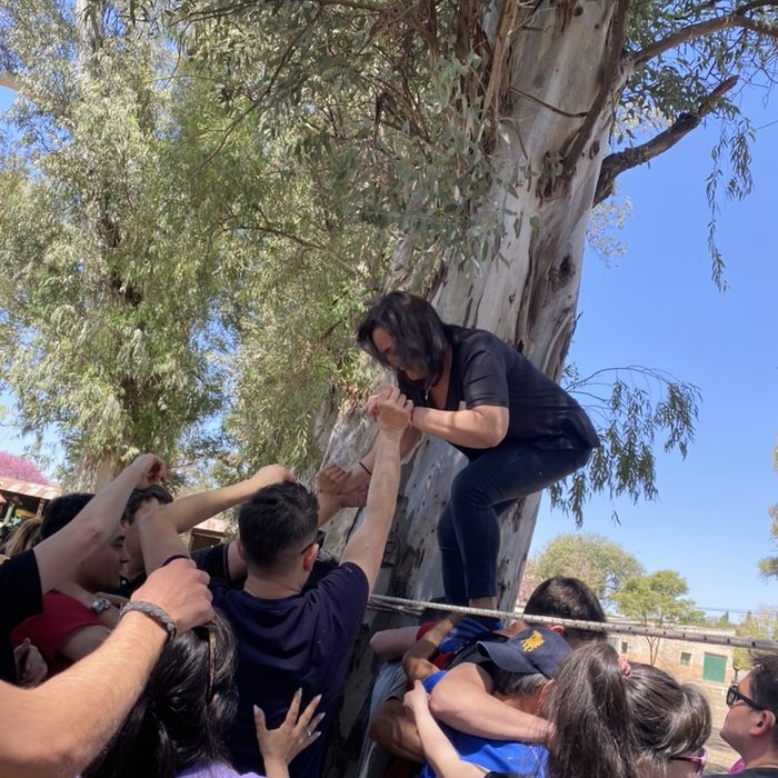 El grupo sostiene a una compañera mientras cruza la soga apoyada en un árbol
